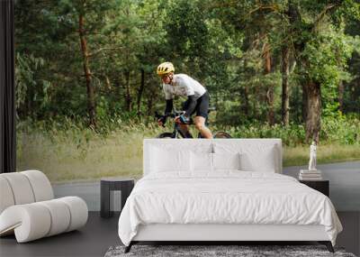 Male cyclist rides a bicycle quickly on an asphalt road in the woods outdoors. The cyclist is training. Wall mural