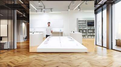 Man walks on a light modern technology store. Choosing gadgets in the electronics store. A modern tech shop with a stylish light interior. Wall mural