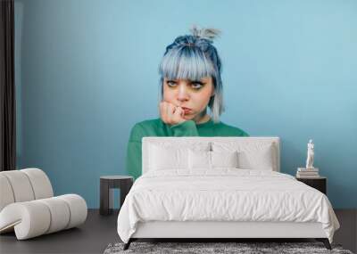 Pensive casual girl with blue hair isolated on blue background, looks away and thinks Wall mural