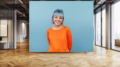 Smiling hipster girl with colored hair stands on a blue background with a happy face and looks at the camera. Wall mural