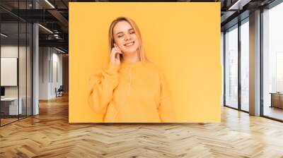 Smiling lady in an orange sweater listens to music in headphones with her eyes closed and a yellow background. The girl music lover listens to her favorite music and buzzing. Isolated. Wall mural