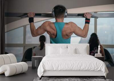 Handsome athlete working out at gym. Pull ups, exercising back. Fitness people. Wall mural