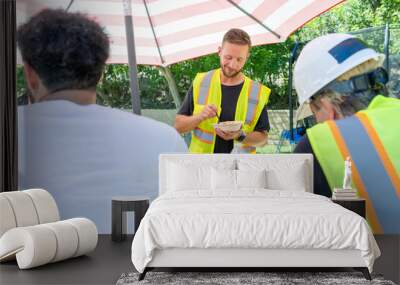 A lively group of men in bright safety vests and helmets enjoy an outdoor meal while enthusiastically discussing plans for a significant house remodeling project and sharing ideas Wall mural