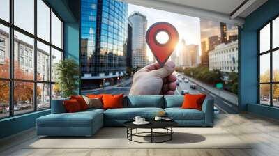 A hand holds a location pin icon against the backdrop of a busy urban street lined with tall buildings. Sunlight shines through the hole in the pin, highlighting the cityscape.AI generated. Wall mural