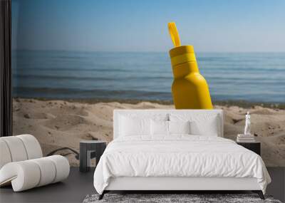 A yellow bottle, thermos standing in the sand on a beach, ocean on sunny summer day. Symbol of summer, holidays and rest Wall mural