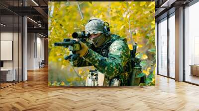 Airsoft man in uniform, stand with sniper rifle on yellow forest backdrop. Soldier aims at the sight Wall mural