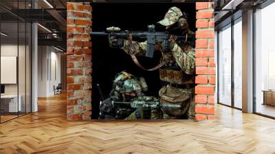 Two men in camouflage cloth green and black uniform with machineguns. Soldiers with muchinegun aims aiming in oposite sides, standing beside wall Wall mural