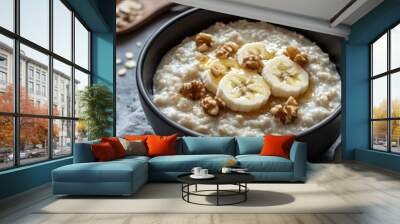 A bowl of oatmeal topped with banana slices and walnuts, served on a textured background. Wall mural