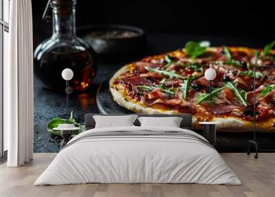 A delicious pizza topped with prosciutto and arugula, alongside olive oil and spices. Wall mural