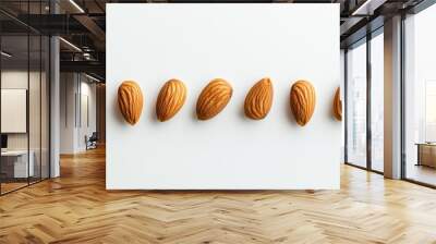 A row of almonds displayed on a white background, showcasing their texture and shape. Wall mural