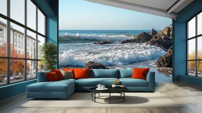 A serene beach scene with waves crashing on rocks under a clear blue sky. Wall mural