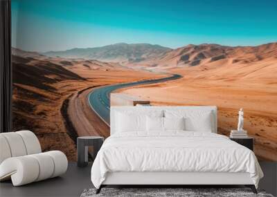 A truck travels along a winding road through a vast, arid landscape with mountains in the distance. Wall mural