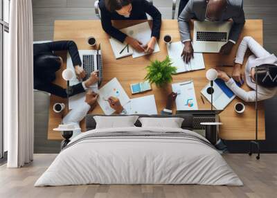 Above view of group of multi ethnic business people working in an office. Team of business people working on project in office, using laptop, writing notes at table with books, sharing learning tasks. Wall mural