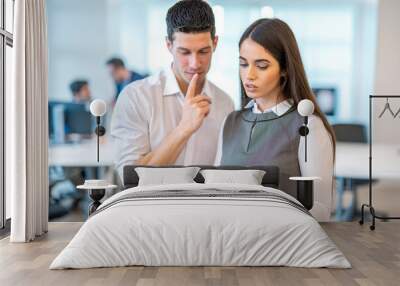 Beautiful business woman showing a contentious document to her handsome colleague, who is thoughtfully pondering a solution as they stand together in the office. Wall mural