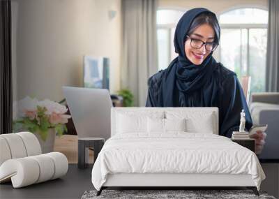 Beautiful happy muslim woman using smart phone and laptop at her luxury home Wall mural