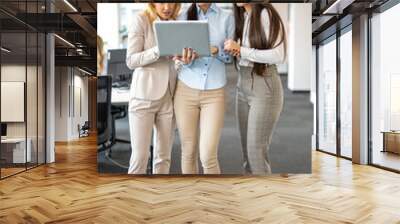 Beautiful multi-aged generation businesswoman standing in office hall, holding laptop and having consultation for business planning financial budget, analyzing marketing data and company's growth. Wall mural