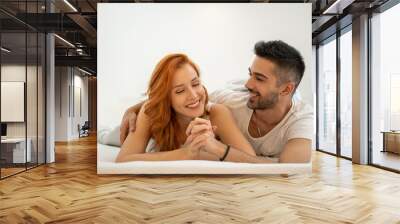 Beautiful smiling couple holding hands while laying together on bed Wall mural