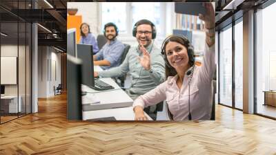 Beautiful woman customer support operator taking a selfie photo of her team colleagues in a call center. Wall mural