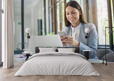 Beautiful young business woman using phone near laptop in office Wall mural