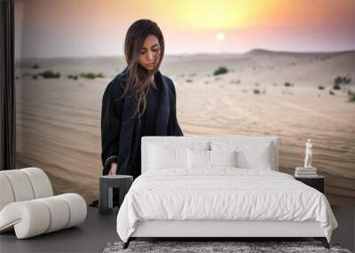 Beautiful young woman in black dress sitting on sand in the desert. Wall mural