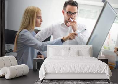 Businesswoman pointing with marker to flipboard and explaining company's financial situation to male pensive colleague Wall mural