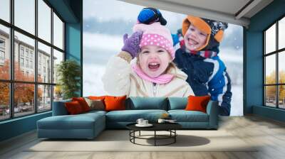 Cheerful children playing on snowy winter day. Little boy taking off hat from cute little girl. Wall mural