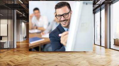 Close up portrait of man in formal-wear and eyeglasses using pen and writing graphs and data on flip chart in front of his business partners at conference or meeting room. Wall mural