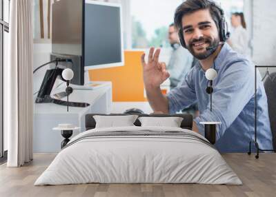 Friendly smiling customer support operator with hands-free headset showing okay gesture in the office Wall mural