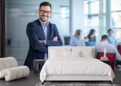 Handsome business CEO executive business man with crossed arms standing in office with colleagues in the background. Wall mural