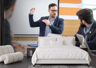 Handsome businessman making presentation for colleagues, explaining business strategy to his team partners in modern boardroom. Wall mural