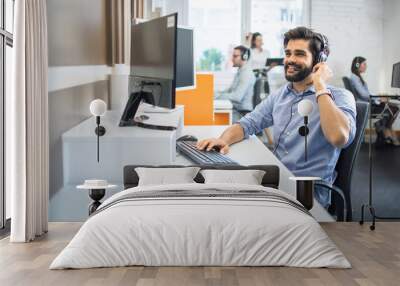 Handsome male employee telephone worker with headset assisting to client while having conversation during online phone call at customer support center. Wall mural