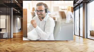 Happy businessman talking on headset in office. Through glass view Wall mural