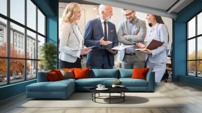 Mature and young businesswomen and businessmen standing in the modern office and analyzing business plan and strategy Wall mural