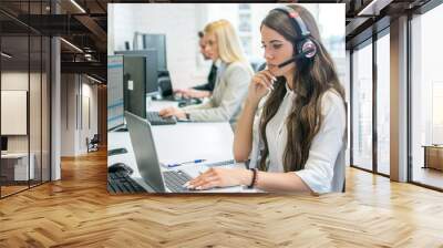 Pensive businesswoman talking on headset while working on laptop in office Wall mural