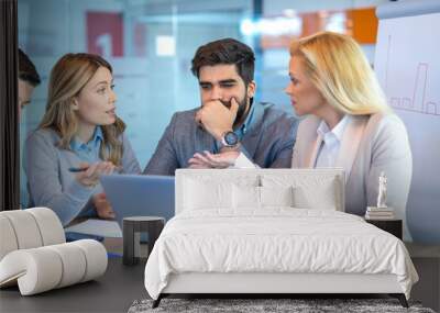 Pensive entrepreneur looking at laptop while his two female colleagues discussing the company's poor financial results during a meeting in the office. Wall mural