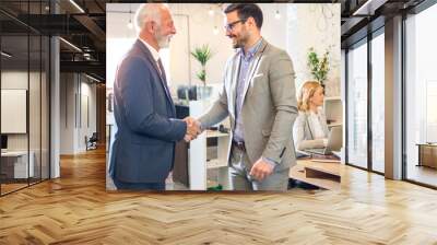 Senior executive shaking hands with young employee at office. Wall mural