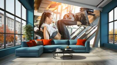 Side view of fit young sportswoman flexing her leg's muscles on exercise machine at the gym during morning workout Wall mural