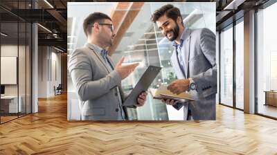 Two handsome businessmen examining documents, talking and smiling while standing in office Wall mural