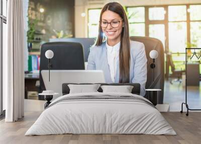 Young businesswoman in formal wear working on laptop in bright office. Wall mural