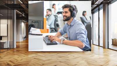 Young handsome man wearing headset working on computer in call center Wall mural