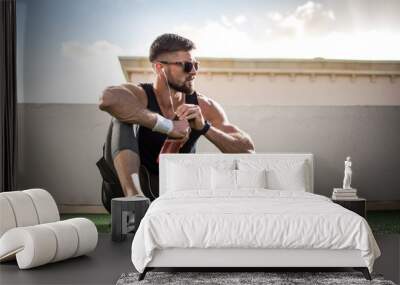 Young man in sports clothing with sunglasses take a break after training at rooftop gym. Wall mural