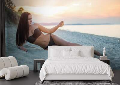 Young sensual woman laying down on beach and playing with sand. Wall mural