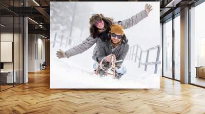 Young happy couple riding sled in snow Wall mural