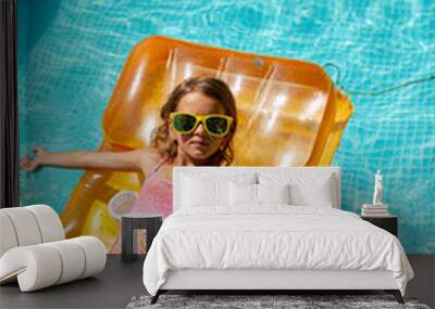 Little girl in sunglasses relaxing in swimming pool, enjoying suntans, swims on inflatable yellow mattres Wall mural