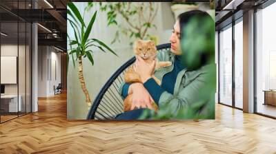 Woman sitting on the armchair holding cute ginger cat Wall mural