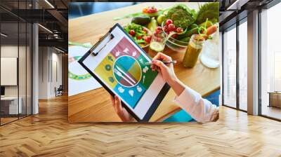 Woman dietitian in medical uniform with tape measure working on a diet plan sitting with different healthy food ingredients in the green office on background. Weight loss and right nutrition concept Wall mural