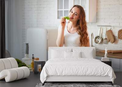 Young happy woman preparing tasty salad in the beautiful kitchen with green fresh ingredients indoors. Healthy food and Dieting concept. Loosing Weight Wall mural