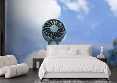 Mini portable blue electric fan. Hand holding bunny look like electric fan in blue cloudy background. Wall mural