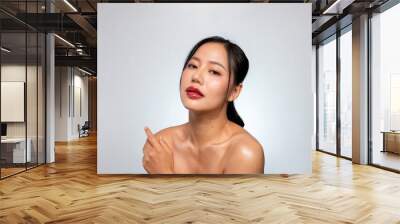 A beautiful Asian woman with glowing tanned skin poses against an isolated grey studio background Wall mural