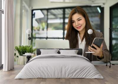 A businesswoman holding her smartphone while working on her work on laptop Wall mural